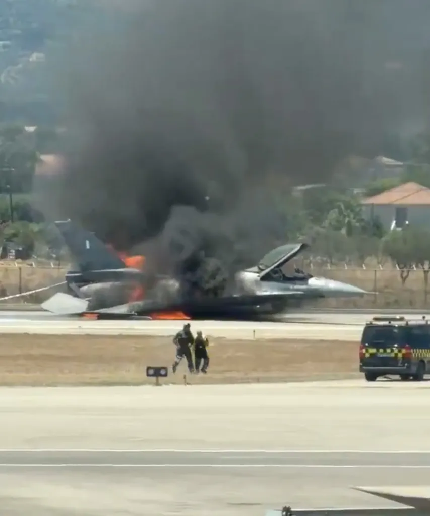 Yunan Hava Kuvvetleri'ne ait F-16 savaş uçağı pistte alevler içinde, iki itfaiyeci yaklaşıyor.