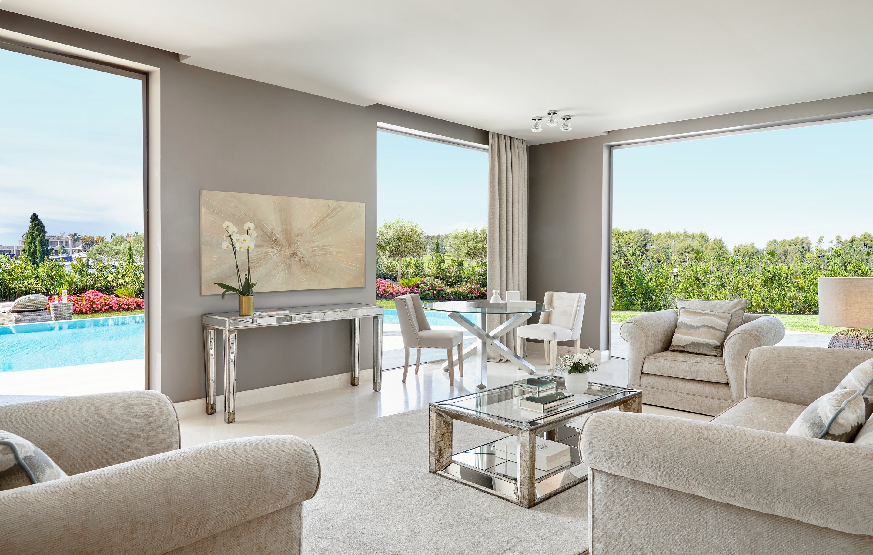 Rahat koltuklar, cam sehpa ve havuz ile yemyeşil bitki örtüsü manzaralı büyük pencereleri olan lüks otel süiti