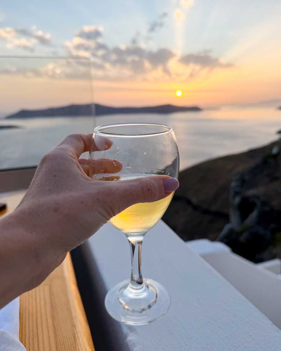 Santorini'de gün batımında şarap kadehi tutan bir el