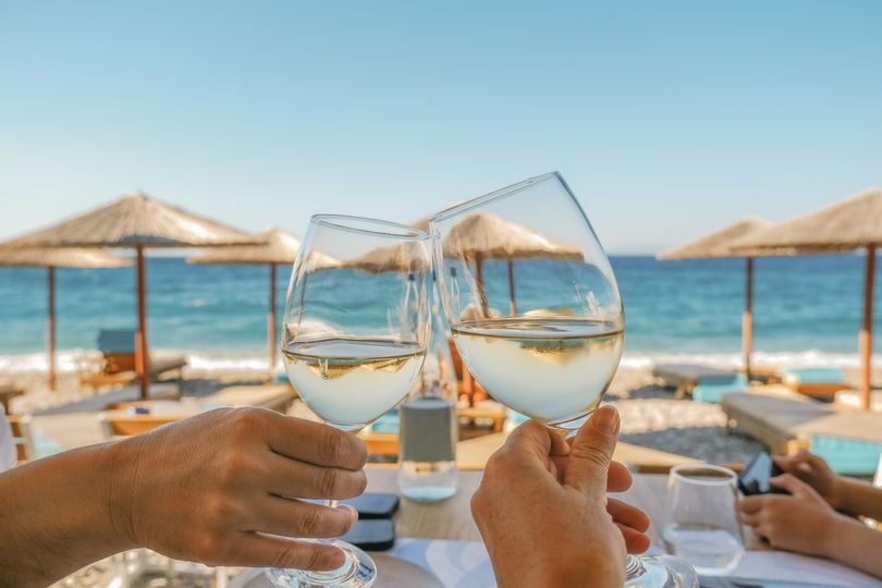 Yunan adasındaki bir plaj kulübü restoranında beyaz şarap kadehlerini tokuşturan aile üyelerinin yakın plan görüntüsü