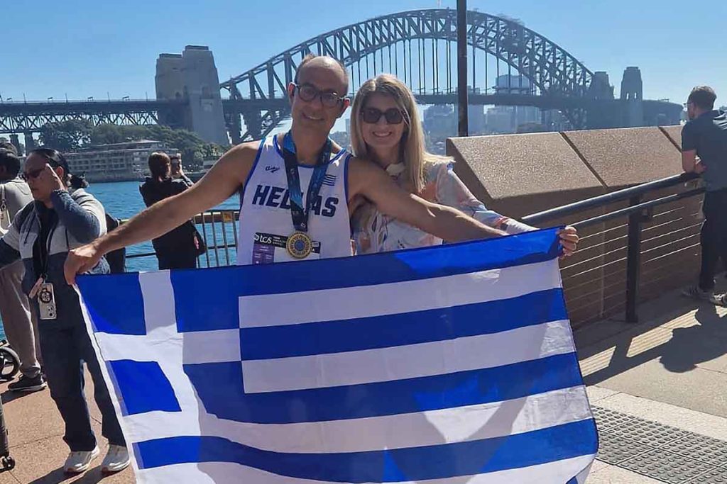 Arka planda Sidney Liman Köprüsü ile bir sporcu, Yunan bayrağı ve altın madalyasıyla poz veriyor.